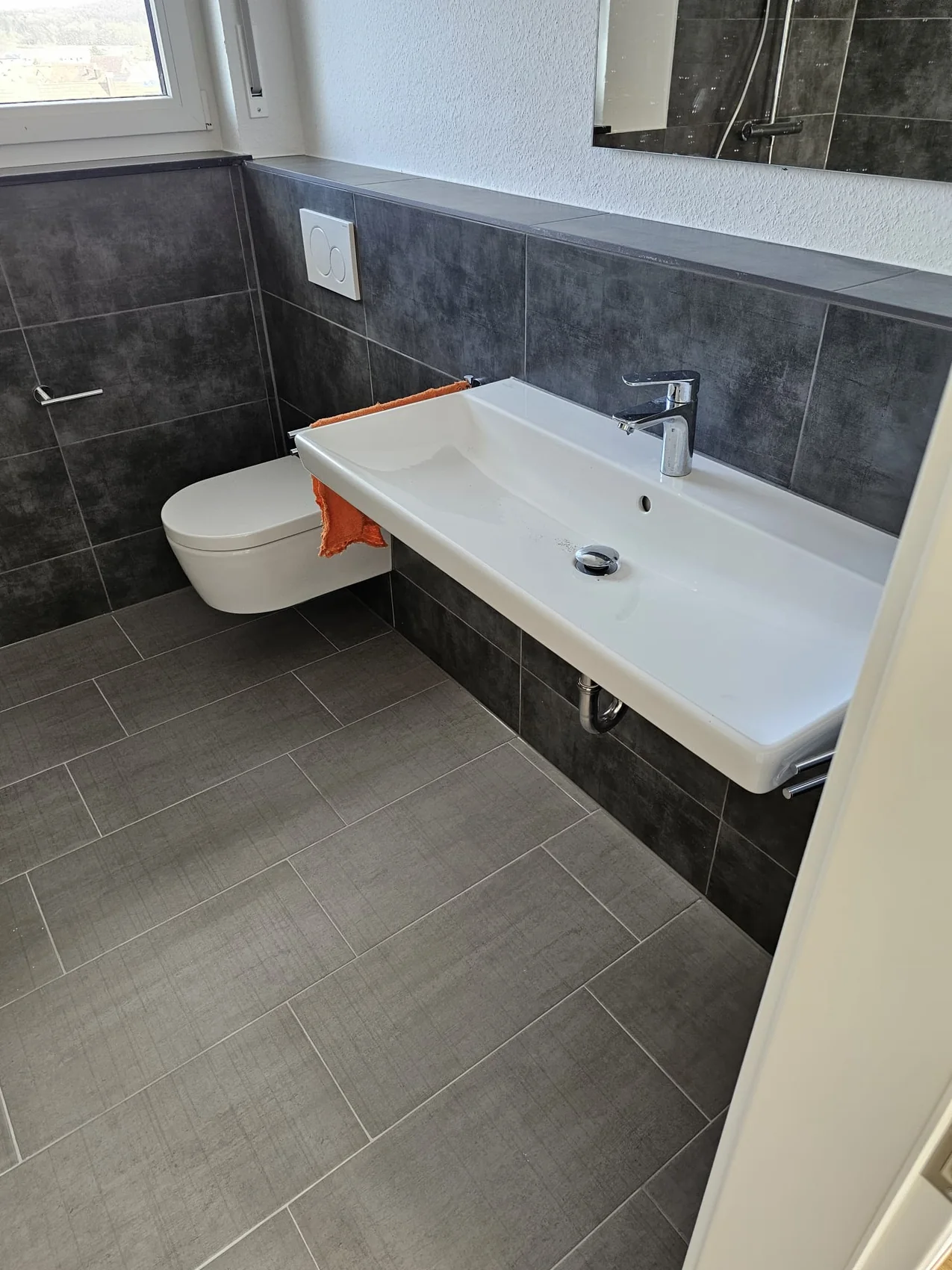 Modernes Bad mit grauen Fliesen, Waschtisch und WC